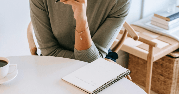 Person writing in a notebook at a desk with coffee