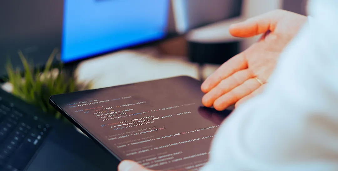 Person holding a tablet showing code next to a laptop